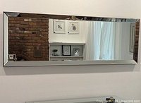 Front view of the rectangular wall mirror reflecting a brick wall and a window with curtains, showing the mirrored glass frame and clean reflective surface.