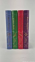 Four leather-bound volumes positioned upright showing spines in blue, green, red and purple