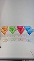 Photo showing all 8 multicolor martini glasses in a row: two orange, two green, two pink and two blue glasses with clear stems and bases