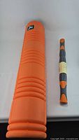 Orange textured foam roller and gray-orange massage stick placed side by side on white background