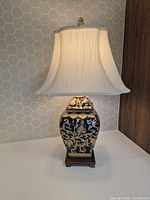 Front view of the custom made table lamp showing the blue and gold ornate patterned ceramic base, fabric shade, and finial on top.