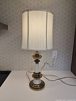 Front view of vintage brass and ceramic table lamp with white and gold finish, showing curved white fabric shade and base in brass and ceramic.