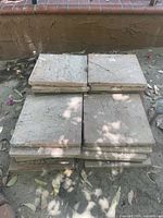 Stack of square concrete outdoor tiles in natural stone color placed outdoors on the ground with some leaves around.