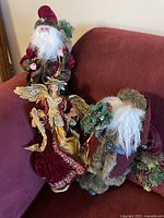 Three holiday figurines on a chair, two Santa Claus and one angel tree topper all detailed with fabric and plastic materials