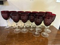 Front view of 14 ruby red and clear cut glass goblets arranged on a wooden surface showing the intricate glass pattern and clear stems.