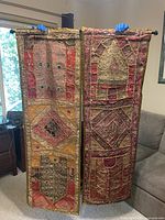 Photo showing both fabric wall tapestries held up side by side, displaying patchwork design with embroidery and beading in multiple colors.