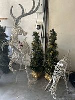 Full view of large reindeer, small reindeer, and two lighted artificial trees with gold bases clustered together indoors.
