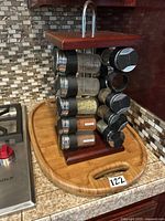 Rotating spice rack loaded with spice jars showing black lids and assorted spices, standing upright on cutting board.