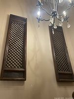 Two dark brown wooden lattice wall panels mounted on a wall beneath a chandelier, showcasing their vertical rectangular shape and lattice design.