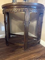 View of medium brown wooden demilune table showing the carved floral pattern on apron and legs, the curved shape and overall condition.