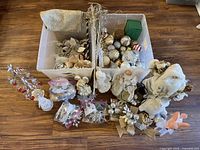 Two clear plastic totes filled with various Christmas and seasonal decorations spread around on a wooden floor
