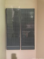 Photo showing two adjacent gray metal wall-mounted file holders with multiple narrow horizontal slots.