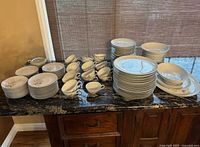 Wide view of entire china set showing head on arrangement of cups, saucers, plates, and bowls in groups on countertop under window.