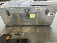 Closed view of large aluminum trunk with latches and lock, showing signs of wear and reinforced corners.