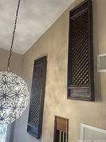 Both rectangular wooden decorative wall panels with intricate lattice design hung vertically on a beige wall near a spherical chandelier light fixture.