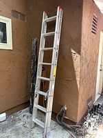 Full view of the aluminum extension ladder leaned against a wall outside, showing the two sections and rungs.