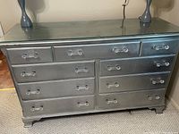 Front view of metallic silver wooden dresser with glass top, showcasing nine drawers and acrylic handles.