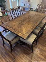 Top and side view of rectangular dark wood dining table with geometric patterned top and matching dining chairs with fabric seats arranged around the table.