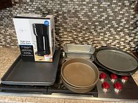 Image showing all baking pans arranged on countertop with Mainstays coffee maker in original box on the left side.