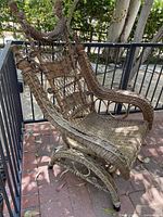 Side angled view of the brown wicker rocking chair showing its woven pattern, curved rockers, and armrest detail.