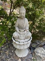 Front view showing seated Buddha on lotus pedestal in outdoor garden setting with foliage background.
