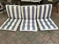 Front view of three gray and white striped outdoor chair cushions laid upright showing vertical stripes and piping edges.
