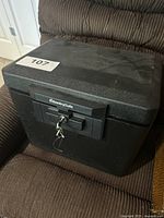 Black SentrySafe security safe closed on a brown chair, key inserted in lock.