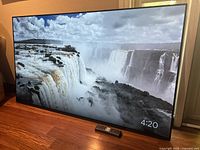 Front view of the television displaying waterfall scenery with remote placed on floor