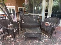 Full view of the four-piece brown wicker furniture set including two single chairs, loveseat/bench, and coffee table on a patio.
