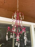 Photo of a vintage chandelier with a pink metal frame, hanging acrylic crystal drops, and four candleholders, shown hanging indoors.