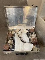 Vintage white leather Riedell roller skates with brown wheels inside a metal case, showing overall condition and included case.