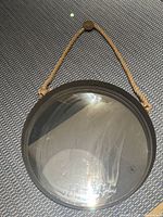 Front view of round mirror showing reflective glass, metal rim, and attached rope hanger.