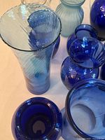 Close-up of several blue glass vases showing varying textures, shapes, and depth of color from light to cobalt blue.