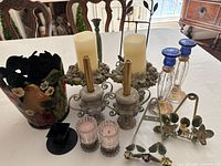 Photo showing various candle holders, painted container, and decorative plate holder arranged on a table.