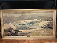 Full frontal photo of framed seascape print showing waves crashing on rocky coastline and cloudy sky. Frame is wood with a gold finish.