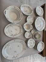 Full view of the main assortment including large oval serving platters, vegetable bowls, cups, small bowls, and round plates showing floral pattern and gold rims.