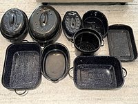 Photo showing multiple black and blue vintage enamelware roasters, pans, and a colander arranged on floor.