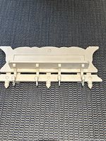 Top down view of vintage wooden wall-mounted shelf with five pegs for hanging items, painted white with decorative shaping along the back panel edges.