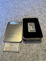 Zippo lighter in original Zippo tin with warranty card visible. Tin lid has text about the Varga Girl lighter history and collectible status.