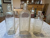 Photo of three antique medicine bottles on a wooden table, varying heights and shape with one embossed bottle.