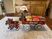 Coca Cola horse-drawn carriage with driver under umbrella, loaded with miniature Coca Cola bottles, horses facing left side on table.