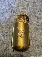 Front view of brass-colored eagle head lighter showing embossed eagle design and missing eye gem on the head.