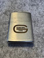 Closed view of a silver-tone Zippo lighter with General Tire logo on front surface.