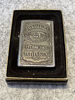 Front embossed detail of Jack Daniel's branding on the Zippo lighter inside the black velvet-lined box.