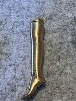 Silver-tone metal lighter shaped like a human leg showing tarnish and wear on a textured grey background.