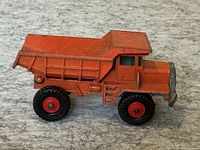 Side view of orange Lesney England Matchbox dump truck showing red-rimmed black tires and tipping bed with some surface wear.