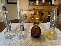Front view of the four oil lamps on a table showing two clear glass lamps, one amber decorative lamp with portraits, one yellow-tinted lamp