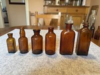 Six antique brown medicine bottles arranged side by side on a wooden surface, showing variation in bottle shape and size.