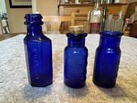 Three cobalt blue glass bottles on table, showing shapes and general condition
