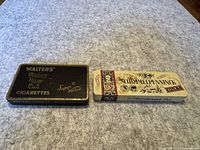 Both tobacco tins side by side on a grey surface showing overall condition and design.